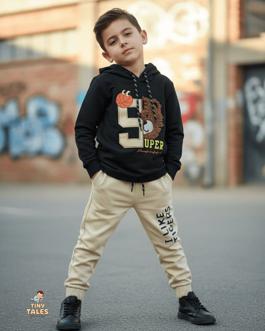 Child wearing a black hoodie with a graphic design and beige pants standing on a street. Tiny Tales baby clothing, Organic baby clothes Pakistan, Premium baby wear, Soft cotton baby rompers, Newborn and toddler outfits, Baby dresses and essentials, Eco-friendly baby fashion, Cute baby clothes online, Safe baby clothing brand, Tiny Tales baby shop