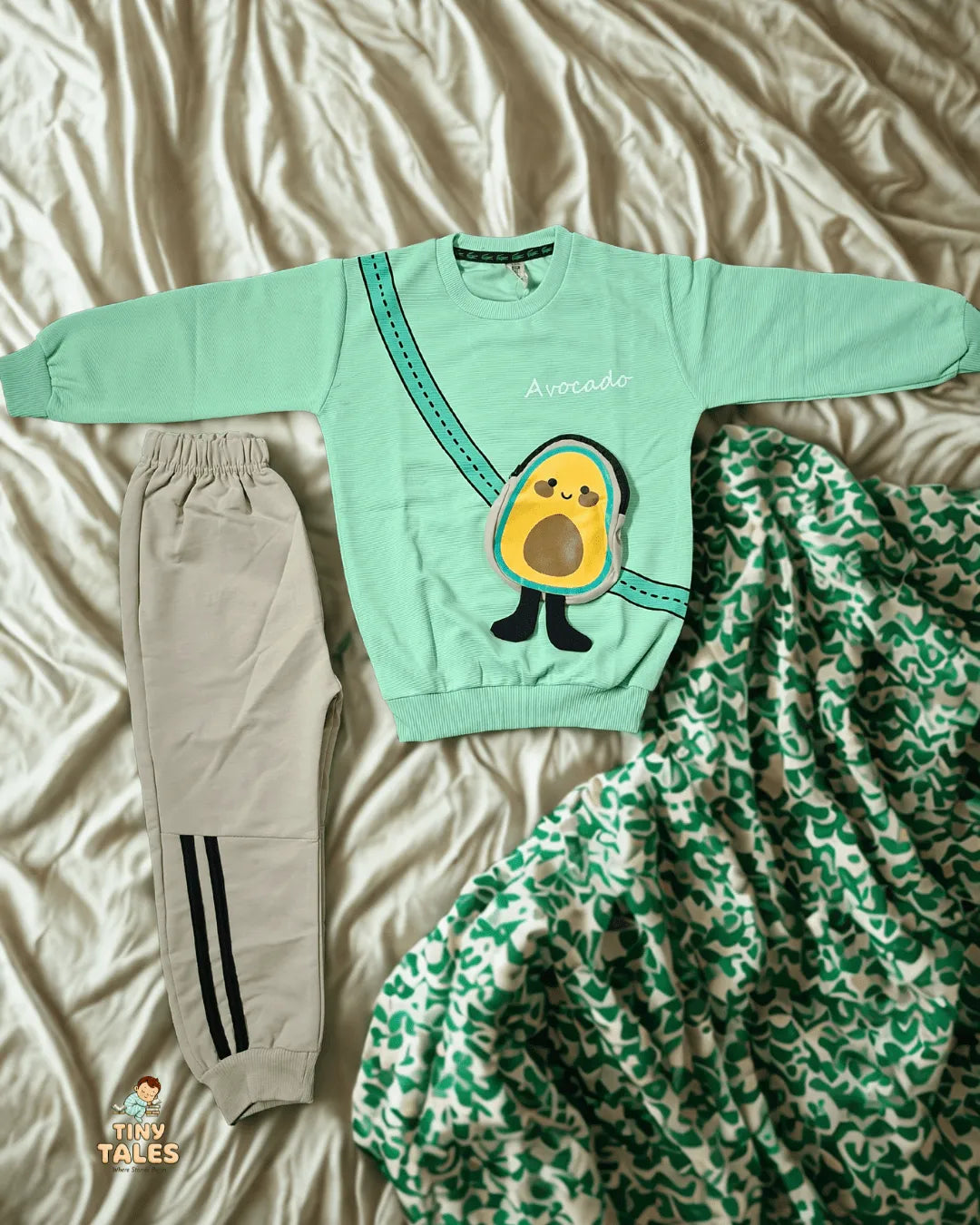 Light green sweatshirt with avocado design and matching pants on a bed