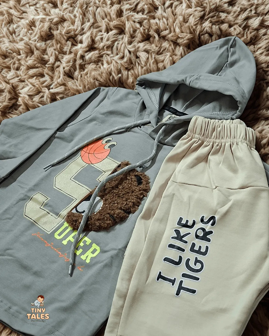 Gray hoodie with a tiger graphic and beige pants with 'I Like Tigers' text on a textured brown surface.