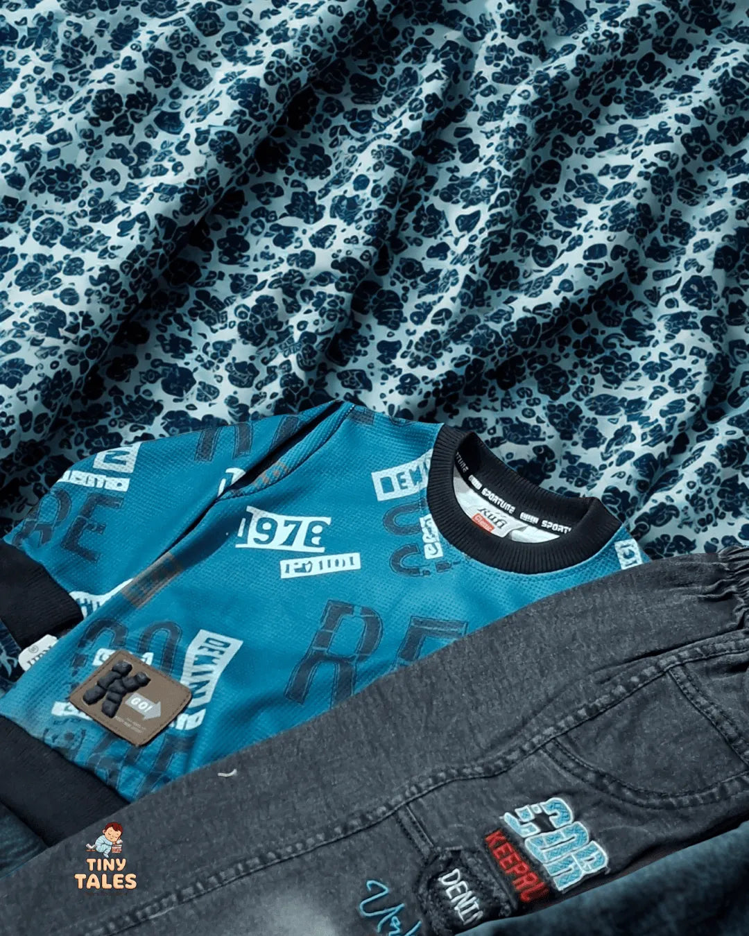 Teal jacket with branding and gray pants with similar branding on a patterned fabric background.